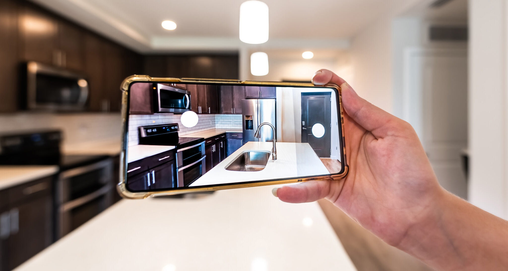 Hand photographing house apartment kitchen island room for sale or rent with phone smartphone closeup point of view in modern luxury condo home with blurry bokeh background